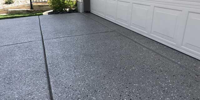 A driveway with a garage; commercial concrete services have been provided to refinish.