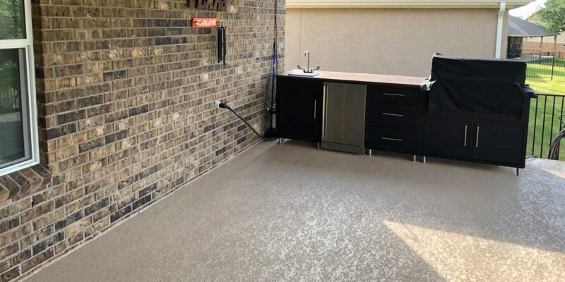 Beige residential concrete flooring on the outdoor terrace with kitchen furniture and brick wall