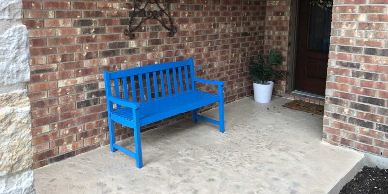 A wooden blue bench on an Austin house porch that has stamped concrete on the floor.