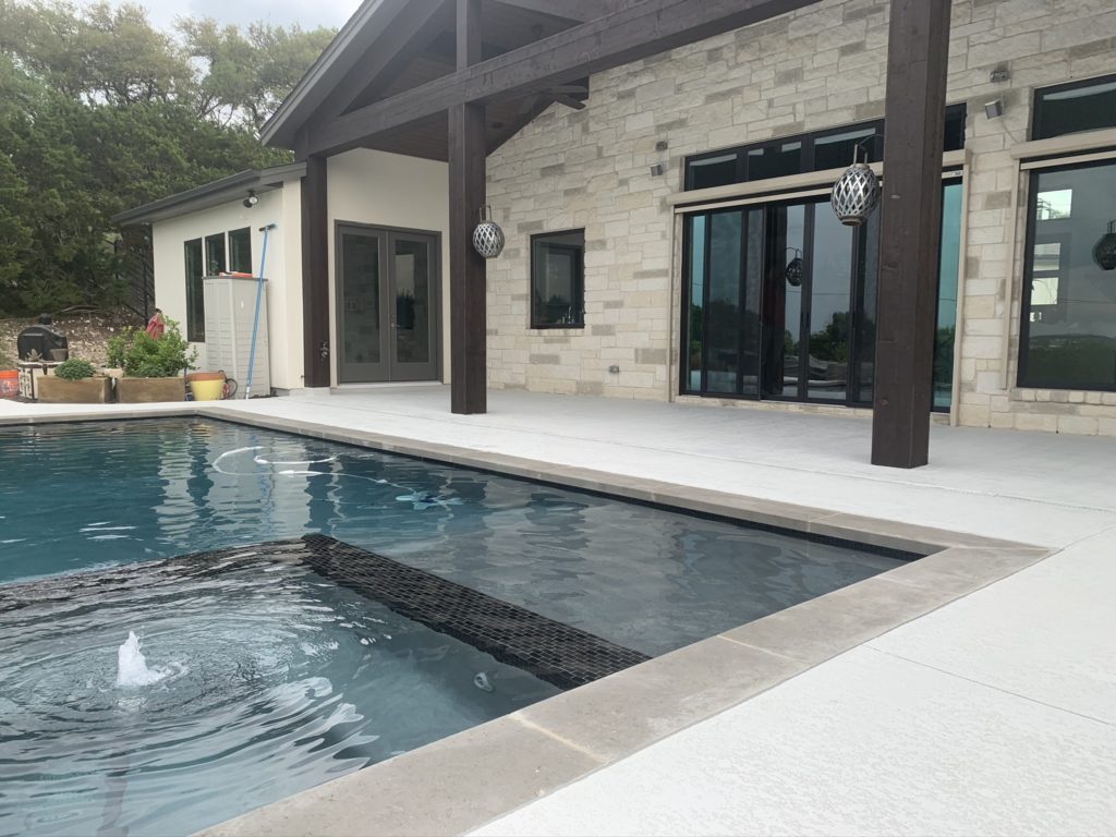 A themed pool area with a fountain and a light-colored cool deck coating concrete patio on the sides